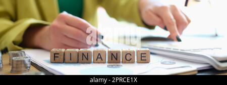 Woman pointing with pen on word finance collected of wooden blocks Stock Photo