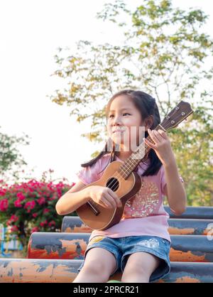 Little asian child girl play the ukulele, in the garden on the Steel pipe Stock Photo