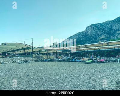 hot, tropical country with sea and mountains. on the beach there are pebbles and small stones. under a stretched awning there are multi-colored soft s Stock Photo