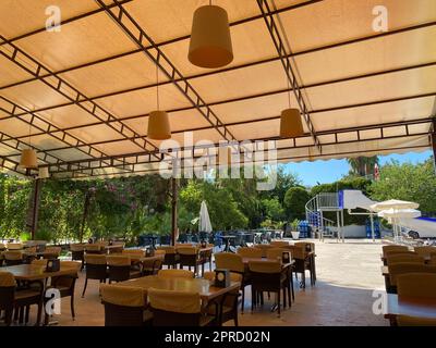 An open cafe with a bar desk with wooden tables and chairs on the street with an open veranda in a tropical warm country at a rest resort with palm tr Stock Photo