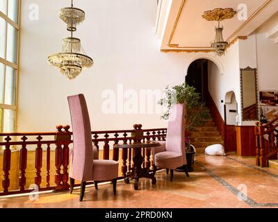 spacious hall with furniture in the hotel. waiting room for tourists, travelers. two pink soft velor armchairs next to a wooden table. Stock Photo