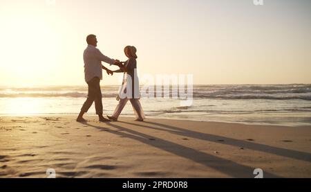 Dance with me darling, will you. Full length shot of an affectionate senior couple dancing together at the beach at sunset. Stock Photo