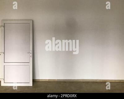 a white plastic door stands on a white plastered wall. indoor renovation. installation of doorways, external and internal decoration. repair door on a Stock Photo