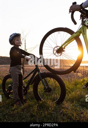 Silhouette of an adult and children's bicycles and a boy in a helmet in the rays of the back sun. Stock Photo