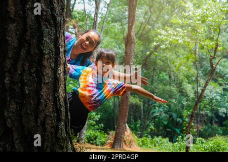 Happy family hiding behind a tree while playing in the park. Happy mother and daughter hiding behind a tree trunk. Green environmentally friendly life Stock Photo