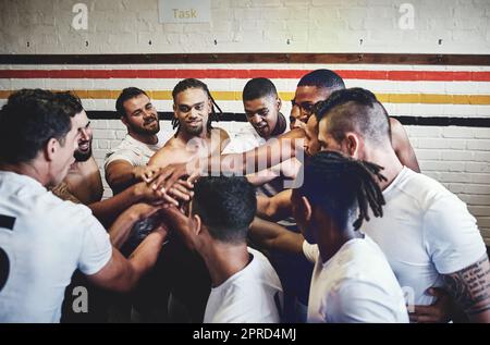 The group of champions. a group of handsome young rugby players standing together in a huddle in a locker room. Stock Photo