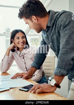 Checking in on how her day is going. two young businesspeople sitting together in the office and going through paperwork. Stock Photo