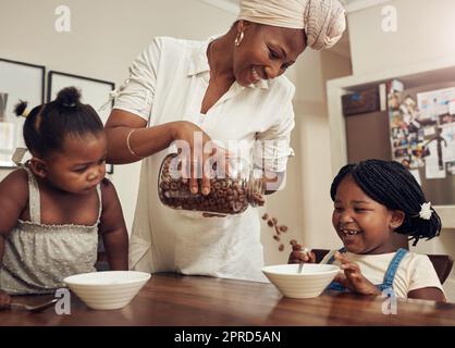 Theyre getting a nutritious and healthy start to the day. a young mother preparing cereal for her two adorable young daughters at home. Stock Photo