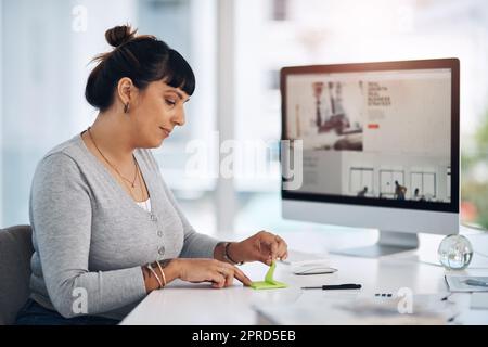 Note-taking is essential to goal setting. an attractive young businesswoman sitting alone in her office and using post-its to make notes. Stock Photo