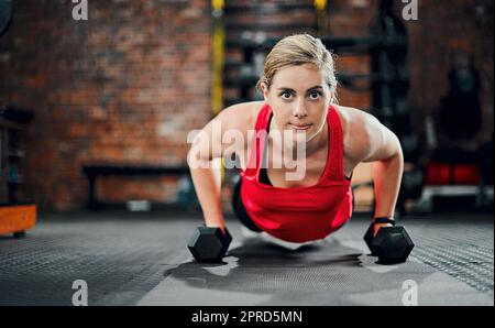 Focused on the end goal. Full length portrait of an attractive young female athlete working out with dumbbells in the gym. Stock Photo