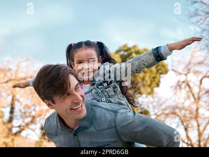 Are you ready for takeoff. an adorable little girl enjoying a piggyback ride with her father at the park. Stock Photo