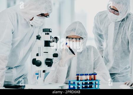 Group of scientists conducting medical research in hazmat suits and protective gloves, for coronavirus cure in a laboratory. Researchers conducting experiments and examining test tube for results. Stock Photo