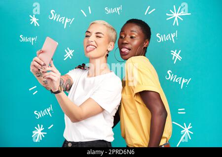 When life gets serious take lots of silly selfies. Studio shot of two young women taking selfies together against a turquoise background. Stock Photo