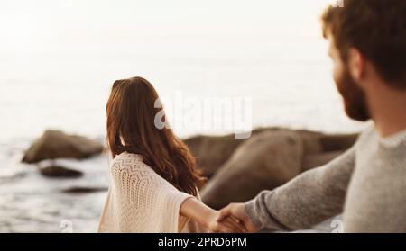 Follow me to paradise. a young woman pulling her boyfriend by the hand while walking on the beach. Stock Photo
