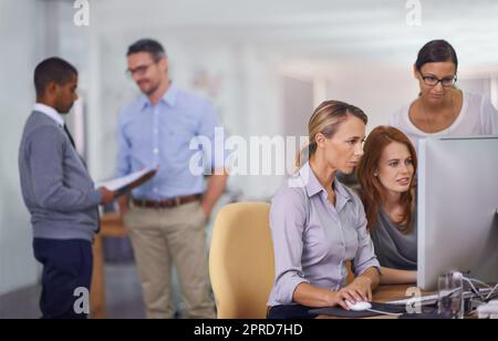 Group of employees at work talking, collaborating, and brainstorming on a computer. Diverse team working together on a project in the office. Marketing agency with busy colleagues browsing technology Stock Photo