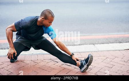 I can never stress the importance of stretching. Full length shot of a handsome young sportsman stretching and warming before exercising outdoors in the city. Stock Photo