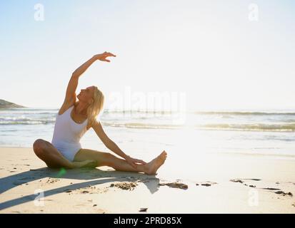 Breathe through the stretches. Full length shot of an attractive young woman doing a yoga stretch early in the morning on the beach. Stock Photo