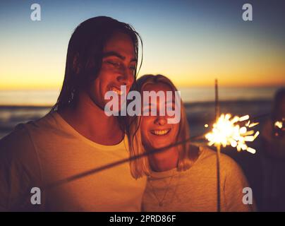 The spark between us will never fade away. a young couple playing with sparklers on the beach at night. Stock Photo