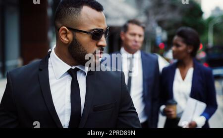 Set your own trends in the business world. a handsome young businessman walking in the city with his colleagues behind him in the background. Stock Photo