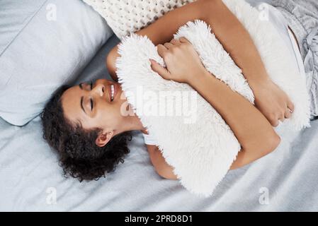 In love with the comfort. an attractive young woman hugging a pillow while lying on her bed at home. Stock Photo