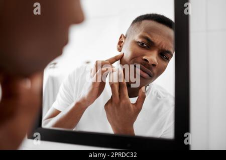 I dont want people to stare at it. a young man squeezing pimples in the bathroom mirror. Stock Photo