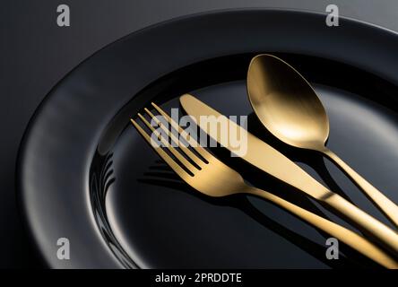 Gold knives, forks and spoons on black plates. Stock Photo