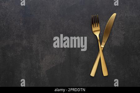 Gold knives and forks set against a black background. Beautiful gold cutlery. Stock Photo