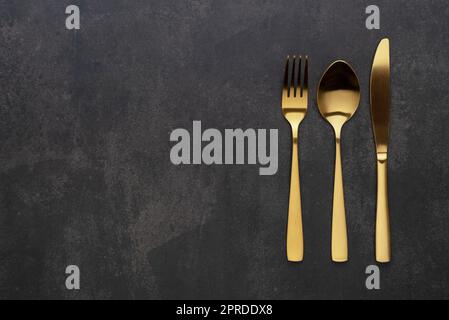 Gold knives, forks and spoons placed on a black background. Beautiful gold cutlery. Stock Photo