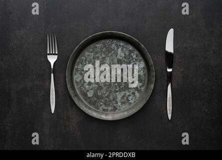 Silver knives and forks on a black background, empty iron plates. Stock Photo