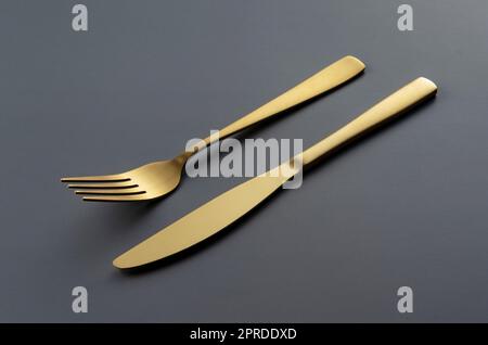 Gold knives and forks set against a black background. Stock Photo