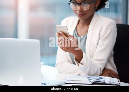 Business woman with a phone texting, browsing and searching social media while working in the office. Creative agent checking schedule list, multitasking and managing goals and tasks on technology Stock Photo