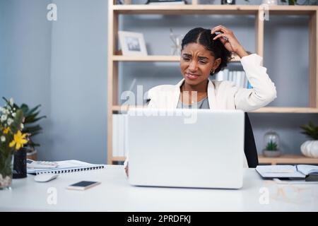 Confused, stressed and angry business woman reading email and scratching her head thinking in her office. A young African American corporate female annoyed while working on a laptop at her workplace Stock Photo