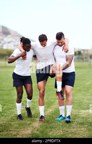 Like soldiers returning from war. young men carrying their team mate off the field after injuring his knee during a rugby game. Stock Photo