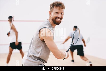Watch me make magic with the ball. Portrait of a young man playing a game of squash with his team mates in the background. Stock Photo