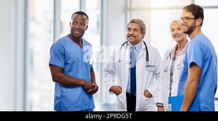Team of happy doctors having a group discussion about professional healthcare together in a hospital. Friendly young and mature medical workers standing together smiling after a successful treatment Stock Photo