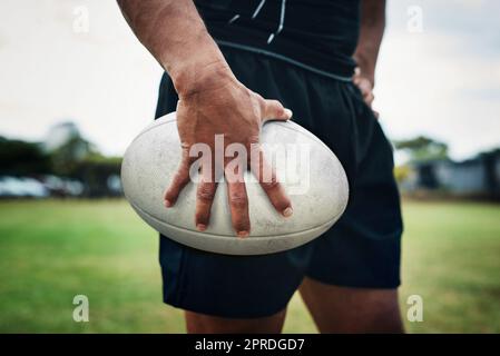 Playing with this ball is his favourite thing. an unrecognizable rugby player holding a rugby ball on the field during the day. Stock Photo