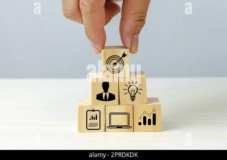 business strategy Action plan Goal and target icons with hand stack a wood cube block on a table. Copy space company development concept. Stock Photo