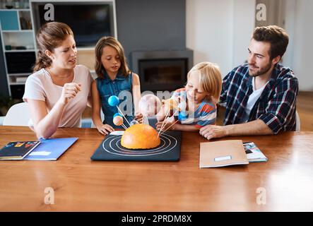 Hes planning on travelling to the moon one day. a beautiful young family working together on a science project at home. Stock Photo