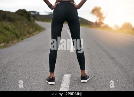 Taking the road less travelled. Rearview shot of an unrecognizable young sportswoman standing with her hands on her hips outside. Stock Photo