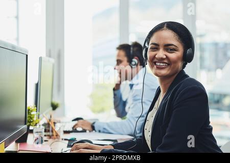 Portrait of happy call center agent working in a busy office, assisting clients and providing good customer service. Young, smiling and cheerful professional excited to offer support or help on calls Stock Photo