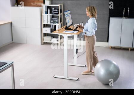 Woman Using Adjustable Height Standing Desk In Office Stock Photo