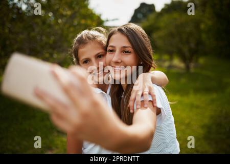 Come take a selfie with me. two young sisters taking selfies in the park. Stock Photo