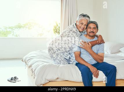 Weve been together through think and thin. Portrait of a cheerful mature couple holding each other while being seated on a bed at home during the day. Stock Photo