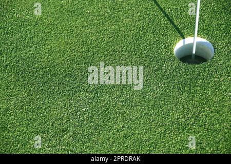 A rich green golf green as a background with a hole as a target. The lawn is cut short and the hole is marked with a flag. The sport is very popular. Stock Photo