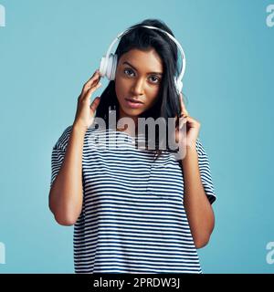 Music is who I am. a beautiful young woman wearing headphones against a blue background. Stock Photo