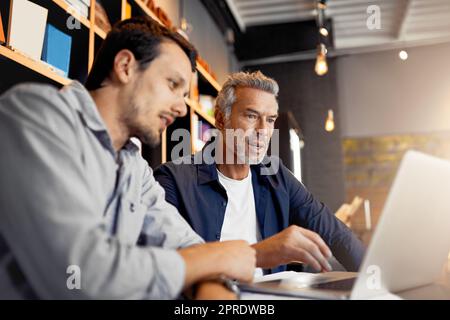 Putting in some extra work over the weekend. two handsome businessmen working together in a local internet cafe. Stock Photo