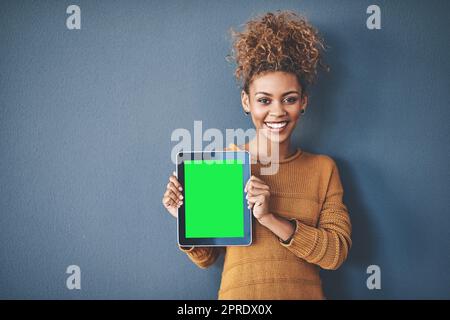 African female holding green screen tablet copyspace. Cute, attractive and smiling young afro woman standing and showing a mobile device.Happy, cheerful and ethnic woman after buying new app. Stock Photo
