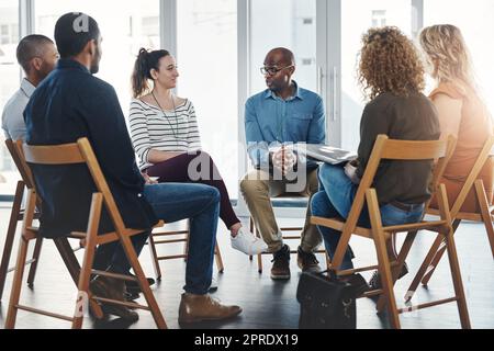 A group therapy session with diverse people sharing their sad problems and stories. People sitting in a circle talking about their mental health issues and looking for support, help and counseling Stock Photo
