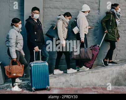 Traveling people wearing covid face mask and suitcases waiting in line or queue at the airport departure or arrival during a global coronavirus pandemic. Immigration of foreign tourists in quarantine Stock Photo