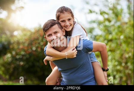 Lets go for an adventure. Portrait of a cheerful young man giving his daughter a piggyback ride outside in a park during the day. Stock Photo